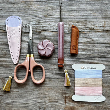 Scissors with sheath, spool of thread, and leather items on a wooden surface