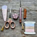 Scissors with sheath, spool of thread, and leather items on a wooden surface