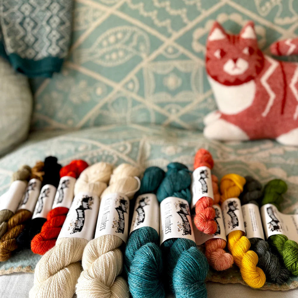 Colorful yarn skeins on a textured surface with a cat-themed pillow in the background