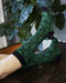 Green and black patterned socks on a wooden surface with a plant in the background