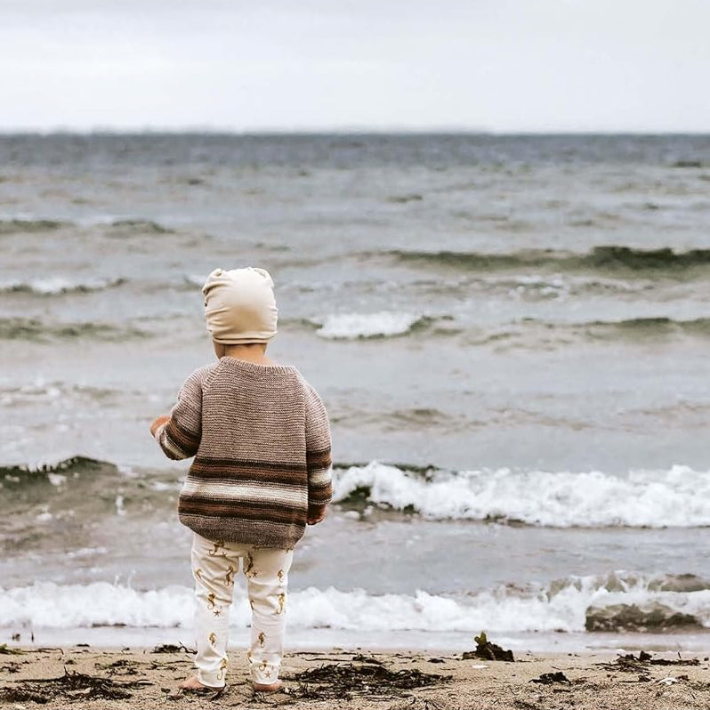 Child standing on a beach looking out at the ocean