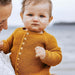 Baby wearing a mustard yellow cardigan held by a person 