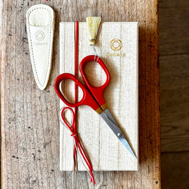 Red scissors with a white sheath on a wooden surface