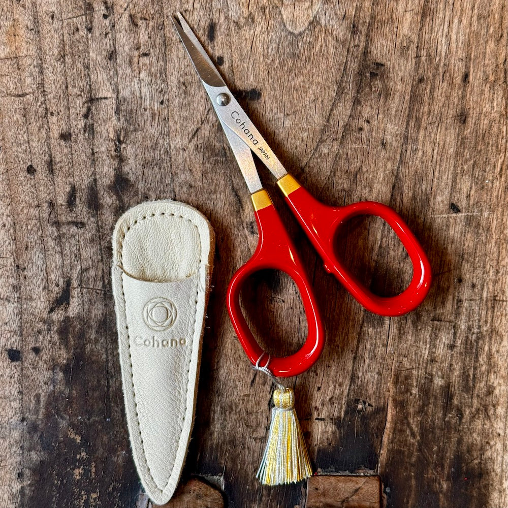 Red scissors with a tassel and sheath on a wooden surface