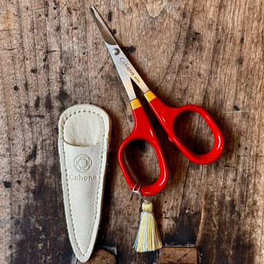 Red scissors with a tassel and sheath on a wooden surface
