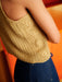 Person wearing a beige crochet top and blue jeans against an orange background