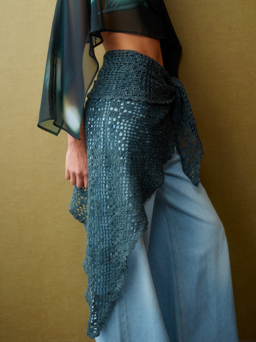 Person wearing a textured blue top and light blue pants against a brown background