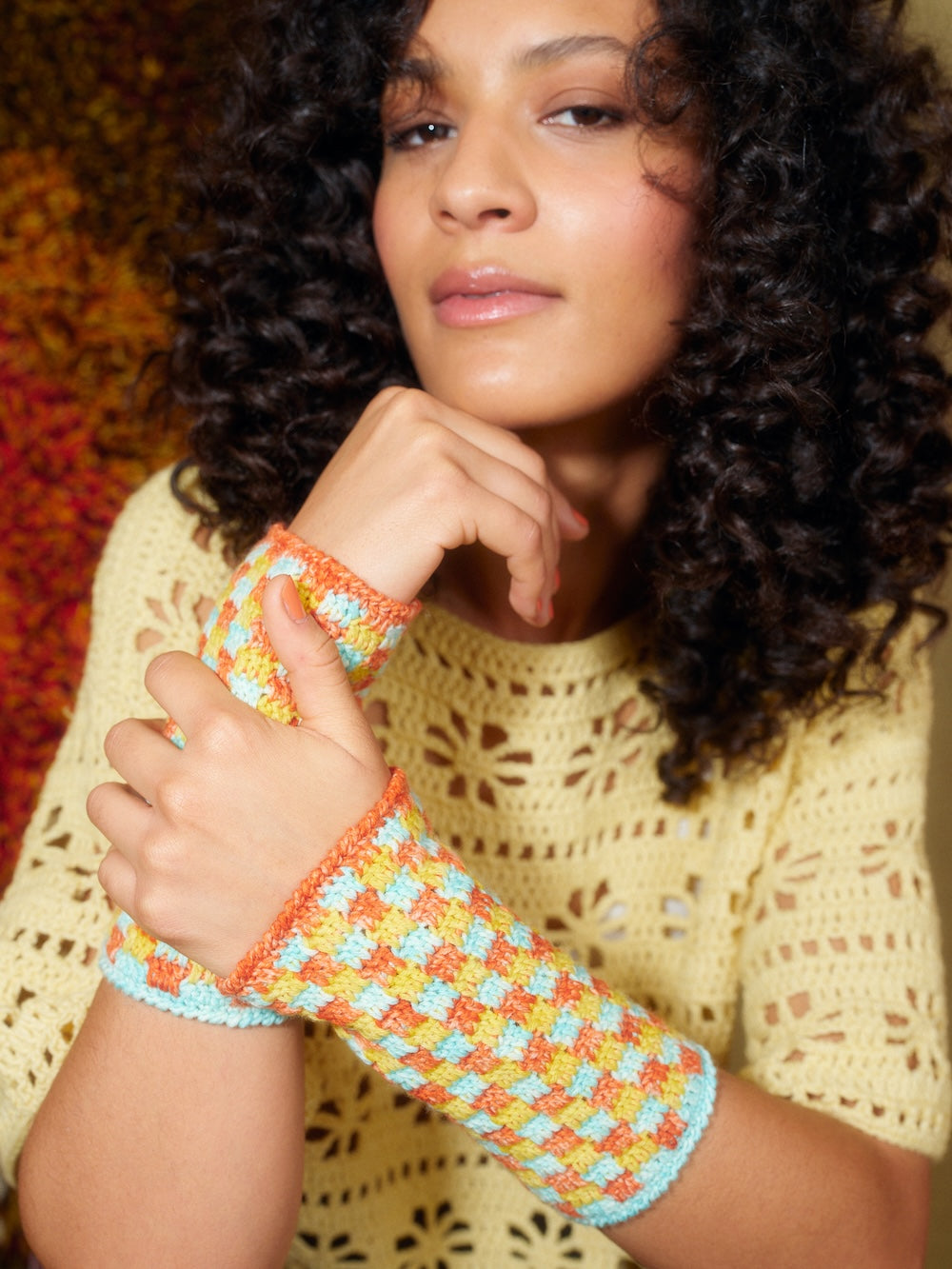 Woman wearing a colorful crocheted wristband against a textured background
