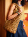 Person holding a woven bag with a wooden wall background