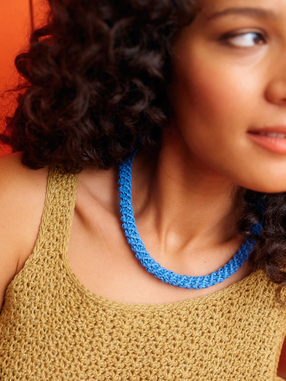 Woman wearing a blue knitted necklace with a neutral background