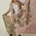 Woman holding a large pink scarf with floral and leopard print patterns against a neutral background