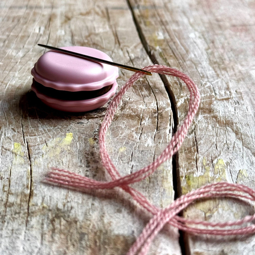 Pink macaron-shaped container with a pink string on a wooden surface