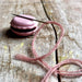 Pink macaron-shaped container with a pink string on a wooden surface