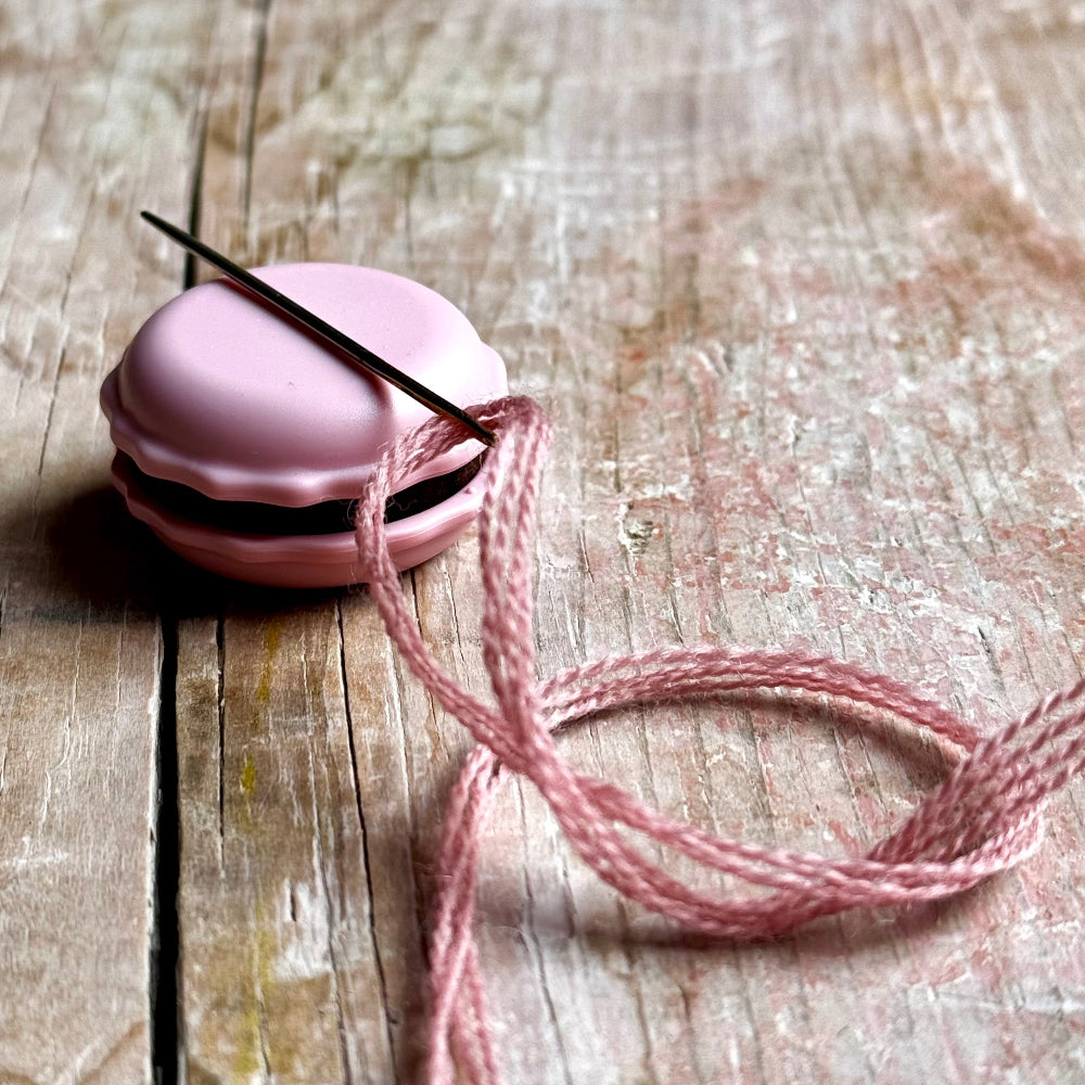 Pink needle magnet with a needle on a wooden surface