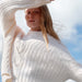 Person wearing a white cable knit sweater with a blurred background