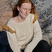 Woman wearing a cream sweater with ruffled shoulders sitting on rocks.