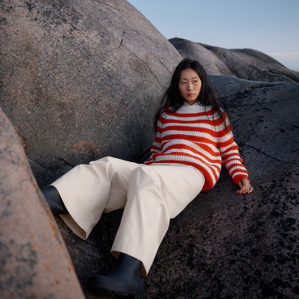 Person wearing a red and white striped sweater sitting on large rocks with a clear sky.