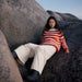 Person wearing a red and white striped sweater sitting on large rocks with a clear sky.