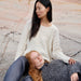 Two women sitting on a stone surface, one wearing a white sweater and the other in gray.