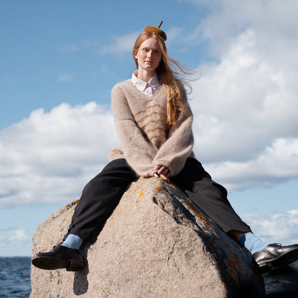 Person sitting on a rock by the sea with a blue sky and clouds in the background