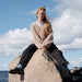 Person sitting on a rock by the sea with a blue sky and clouds in the background