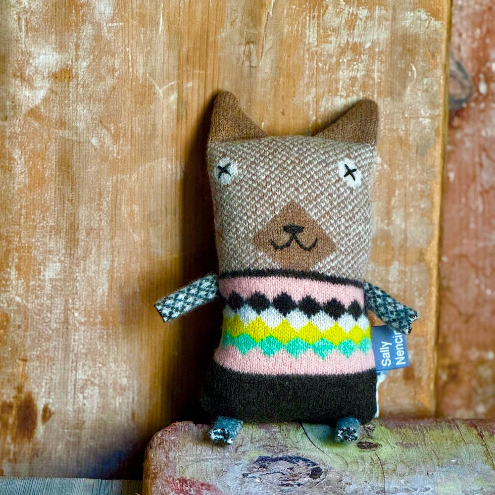 Knitted dog-shaped pillow with a colorful pattern on a wooden surface