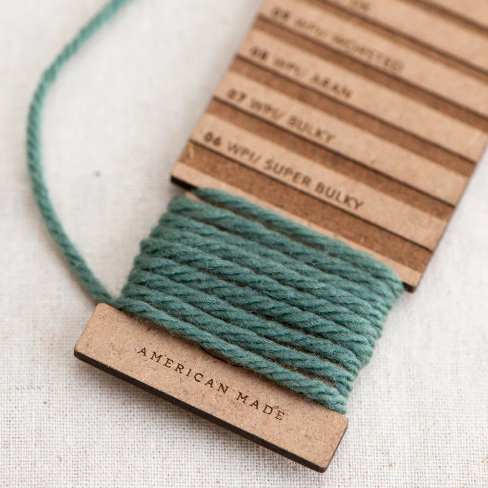 Teal yarn on a cardboard reel with 'American Made' label on a light background
