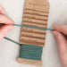 Person holding a skein of teal yarn with a 'twig & horn' label on a light background