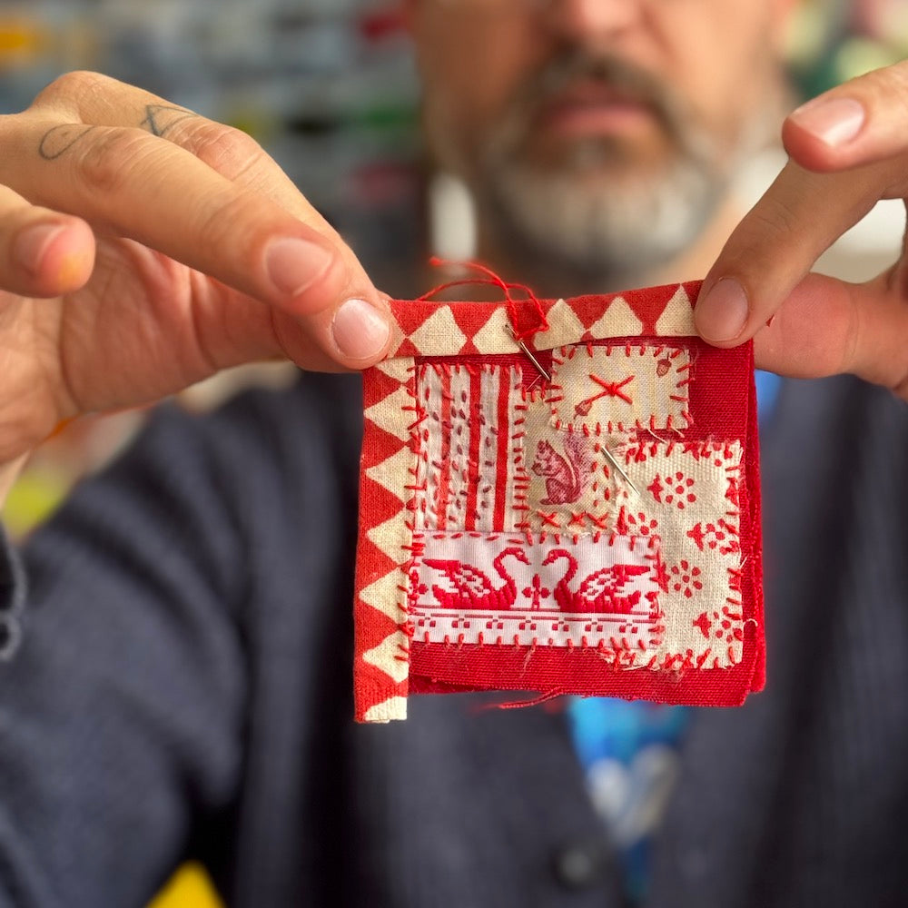 Person holding a red and white embroidered fabric square with a blurred background