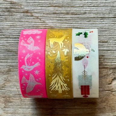 Three rolls of decorative washi tape with festive holiday designs, including birds, deer, and Christmas motifs, displayed on a rustic wooden surface.