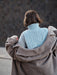Person wearing a light blue knitted sweater with a brown coat over it, standing against a dark background.