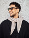 Man wearing sunglasses and a beige scarf against a textured wall