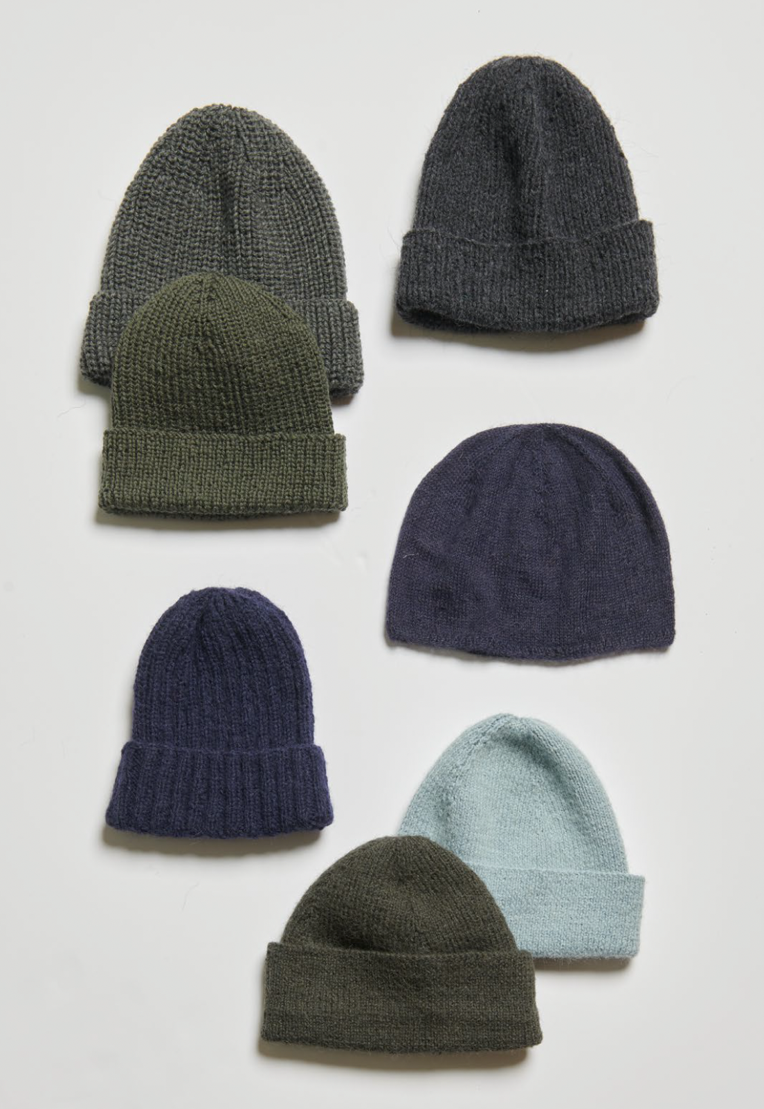 Set of six knit beanie hats in various colors on a light gray background