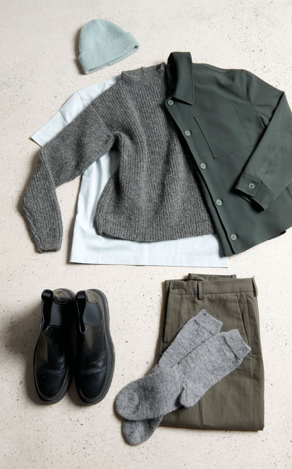 Collection of clothing items including a sweater, jacket, pants, shoes, and socks on a light surface.
