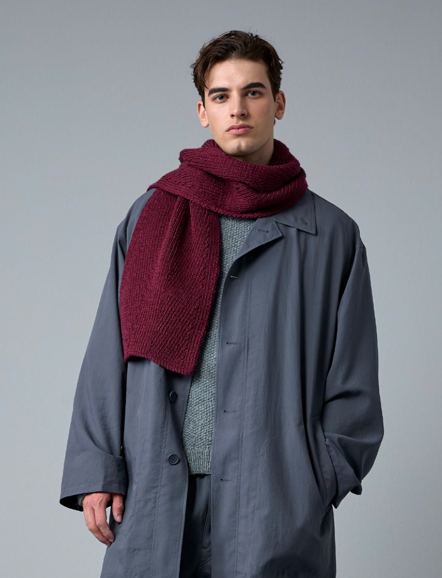 Man wearing a long coat and a red scarf against a gray background