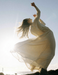 Woman in a white dress standing on a beach with arms raised, sunlit background