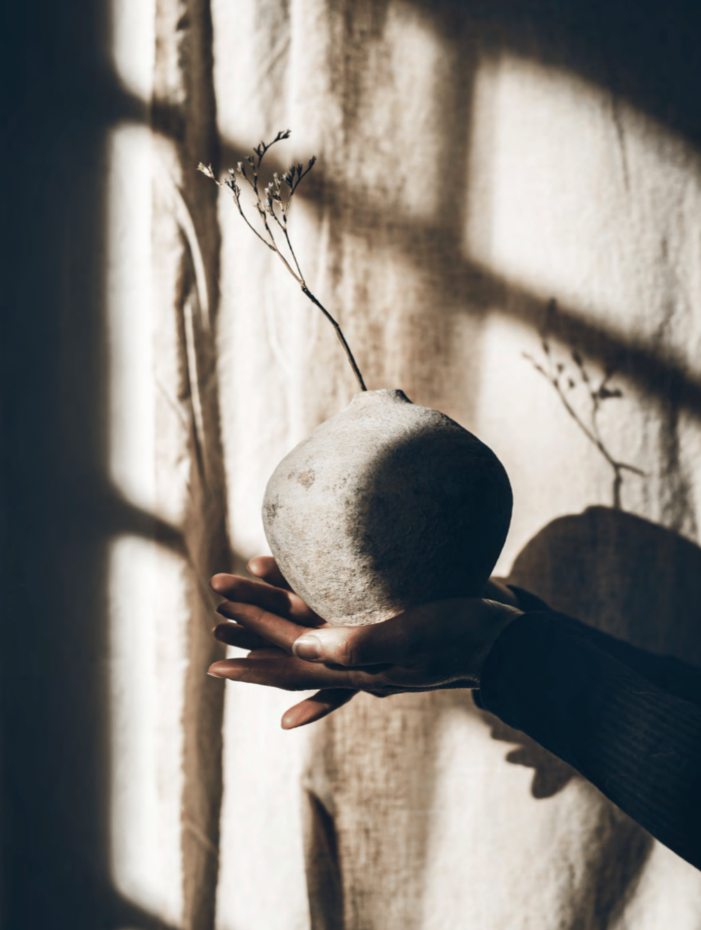 Person holding a textured vase with a plant against a light curtain