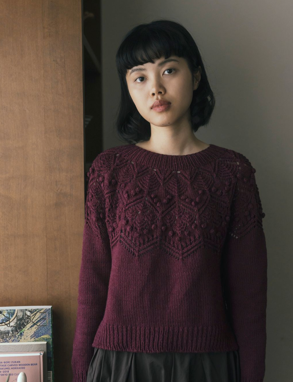Woman wearing a dark purple sweater with intricate patterns against a neutral background