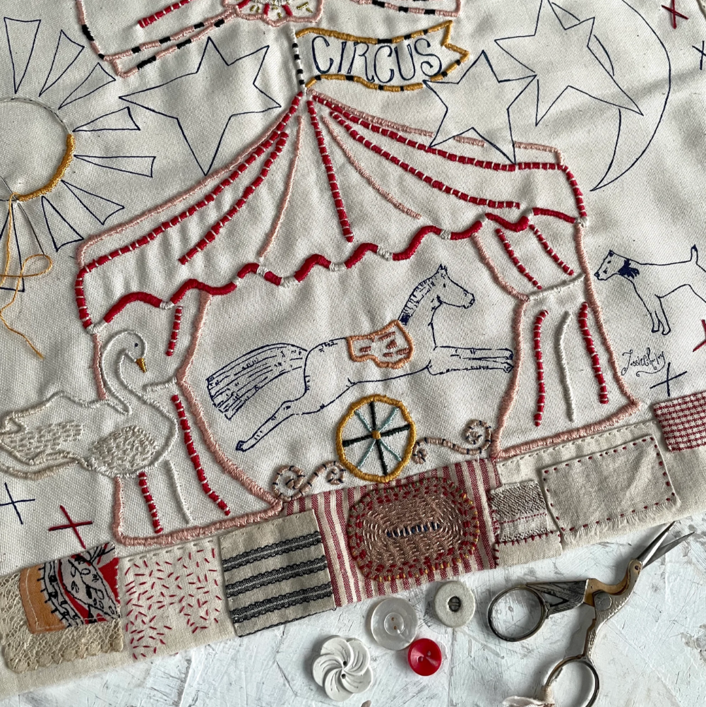 Embroidered design of a circus scene on fabric with scissors and thread.
