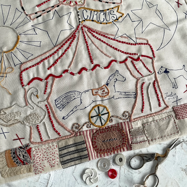 Embroidered design of a circus scene on fabric with scissors and thread.