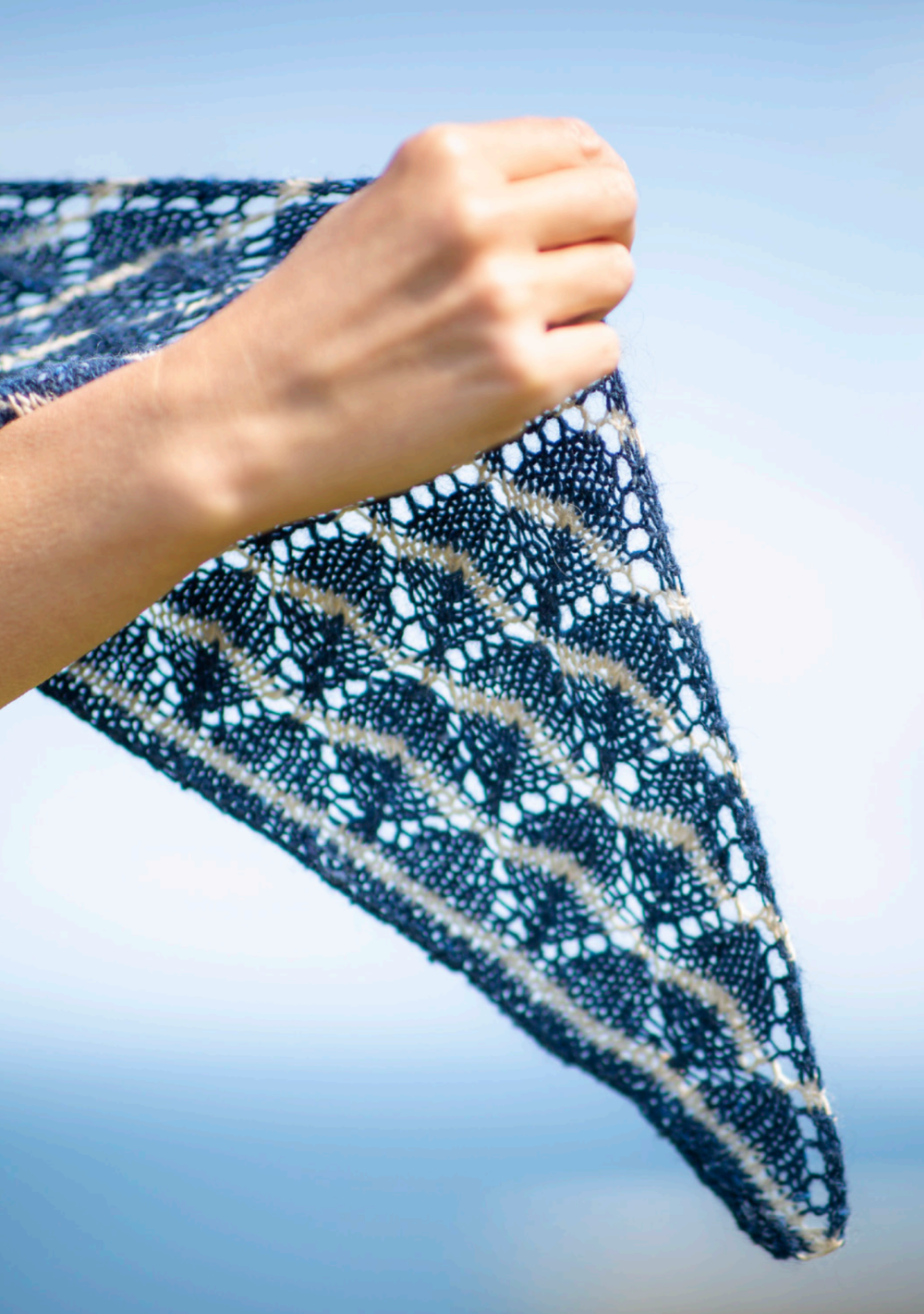 Hand holding a blue and white patterned fabric against a clear blue sky