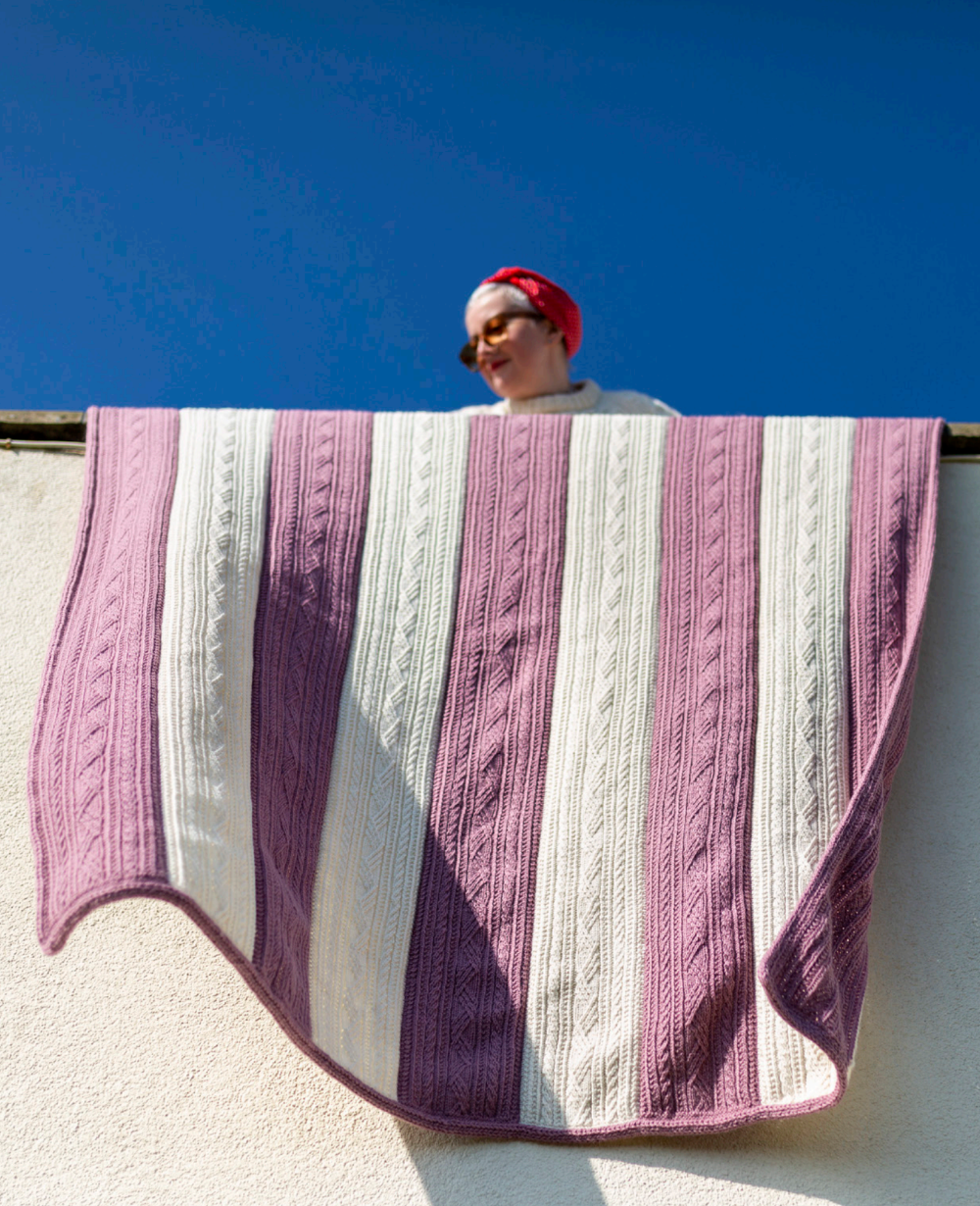 Person holding a striped knitted blanket against a blue sky