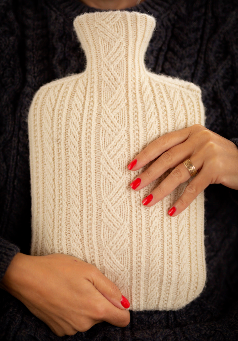Person holding a beige knitted hot water bottle with a dark background