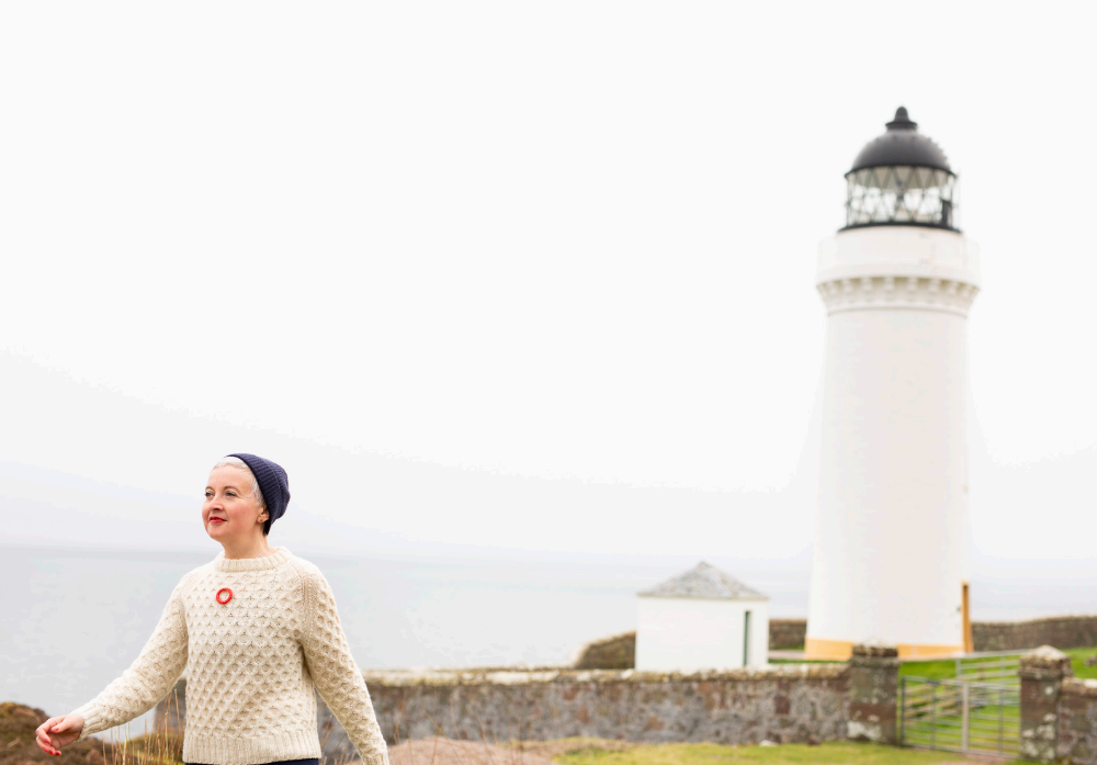 Person standing in front of a lighthouse on a foggy day