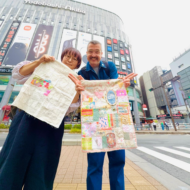 Two people holding colorful fabric panels in front of a modern building with 'Yodobashi-Akiba' branding.