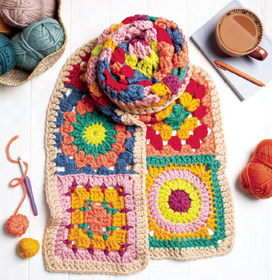 Colorful crocheted blanket with yarn and a cup of coffee on a white surface
