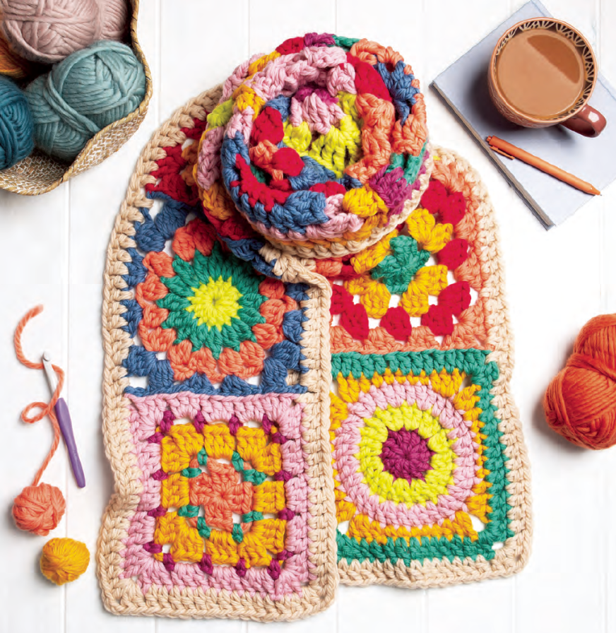 Colorful crocheted blanket with yarn and a cup of coffee on a white surface
