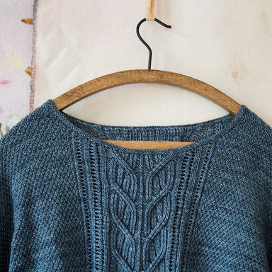 Blue knitted sweater with intricate pattern on a wooden hanger against a light background