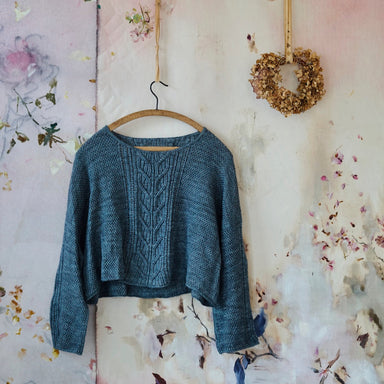 Blue knitted sweater hanging on a floral-patterned wall with a decorative wreath.