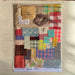 A handmade patchwork fabric kit in a clear plastic sleeve, featuring various colorful fabric squares, plaid patterns, lace, and a brown ribbon on a light wood background.